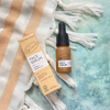 Upcircle face serum bottle and packaging on a textured surface with tassels
